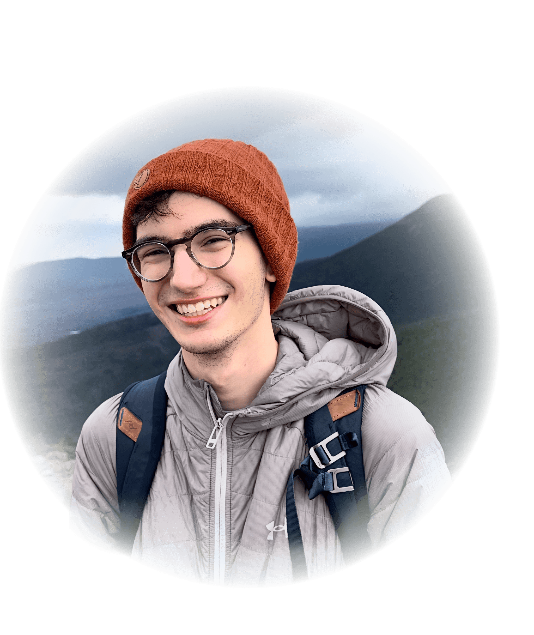 Person smiling wearing a plush beanie and round glasses with a mountain behind them.