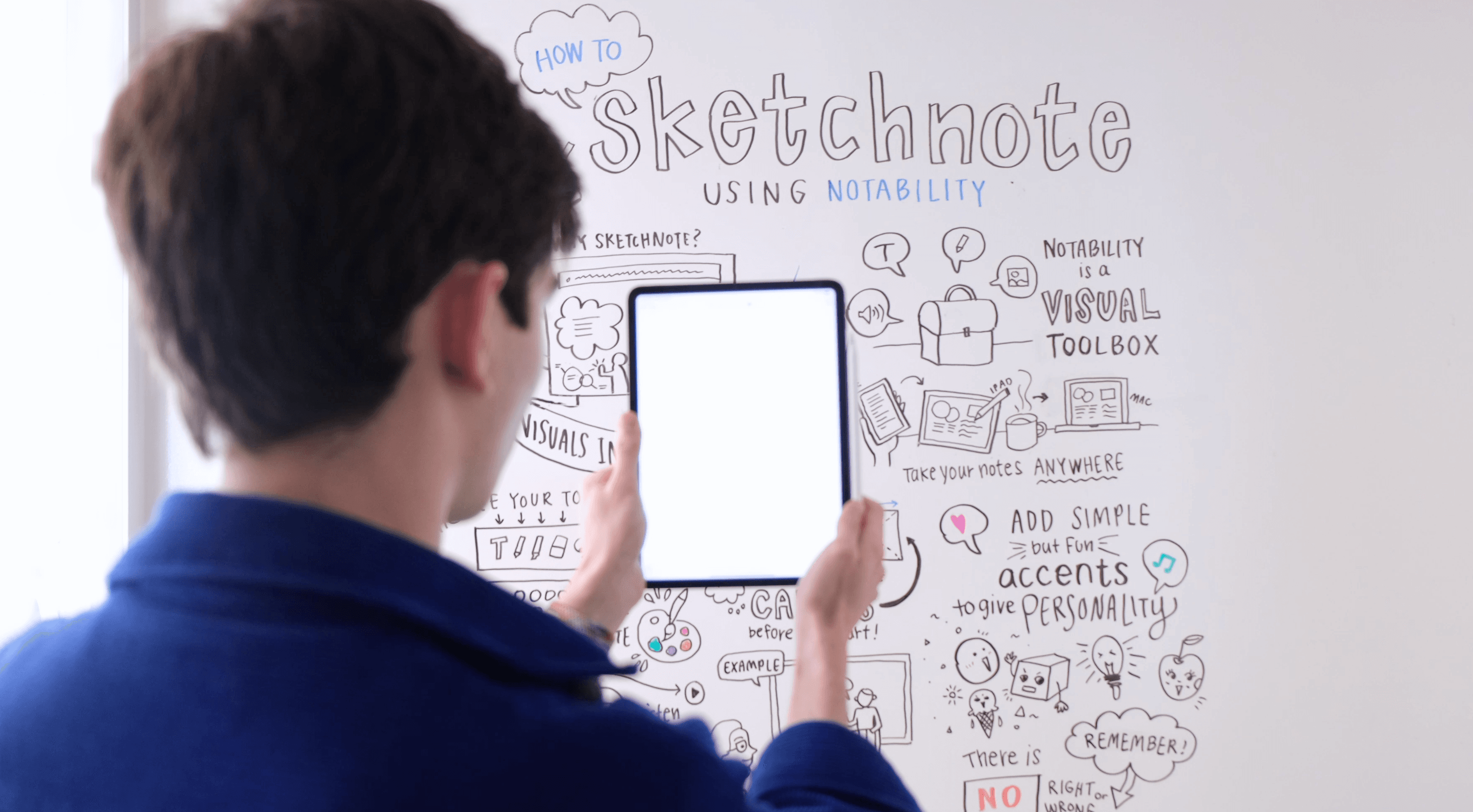 Me wearing a deep blue curduroy shirt holding up an iPad in front of a whiteboard.